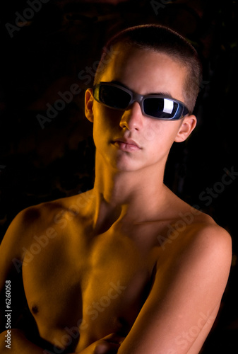 Shirtless teen boy in sunglasses looking tough.