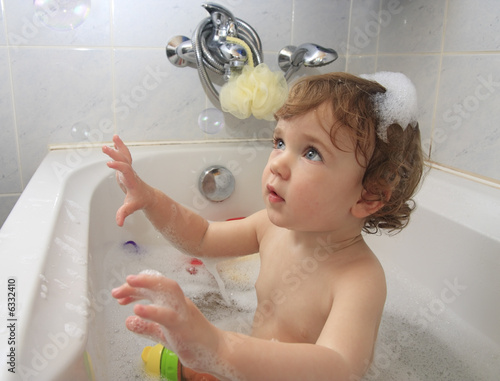 A child playing with soap foam in a bathtub.
