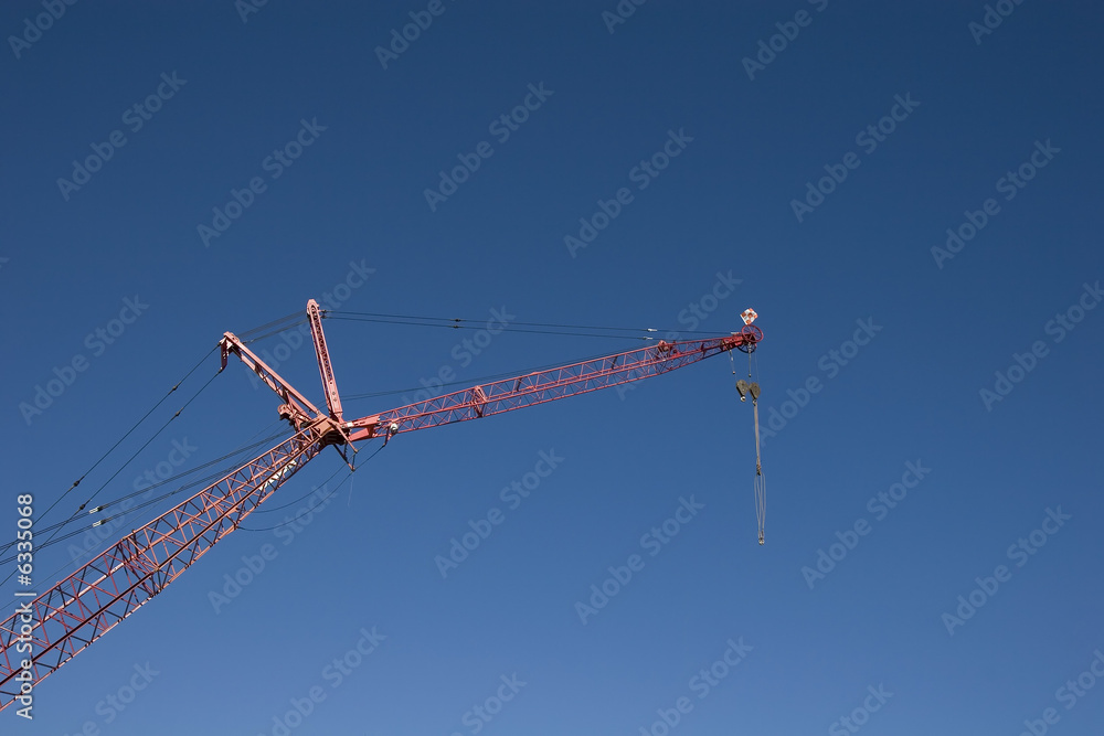 A red crane against a blue sky with a pulley attached A red crane against a blue sky with a pulley attached