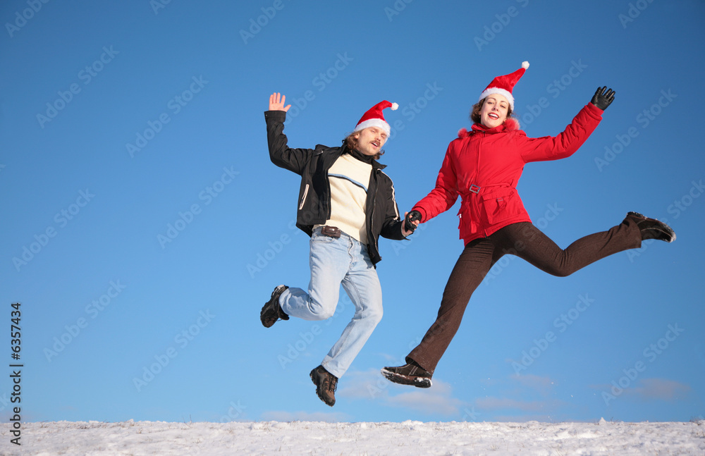 couple jump on snow in santa claus hats