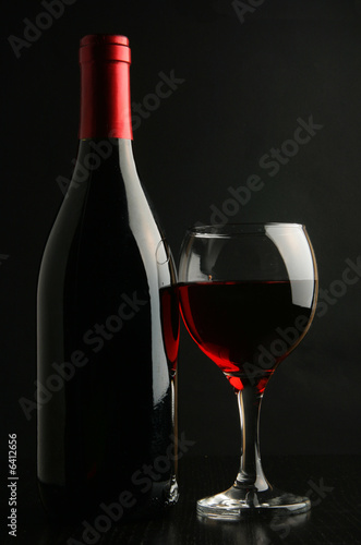 Wine bottle and footed glass over black background