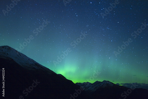 Northern lights making the sky green over the tops of mountains