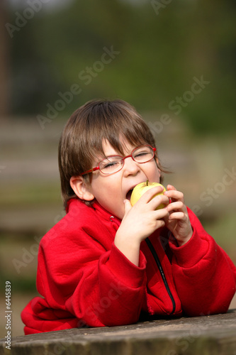 garçon avec des lunettes entrain de manger une pomme