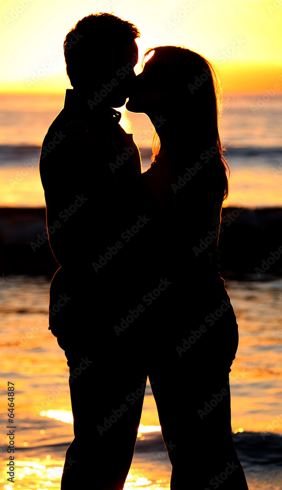 Silhouette of a young couple kissing on the beach at sunset
