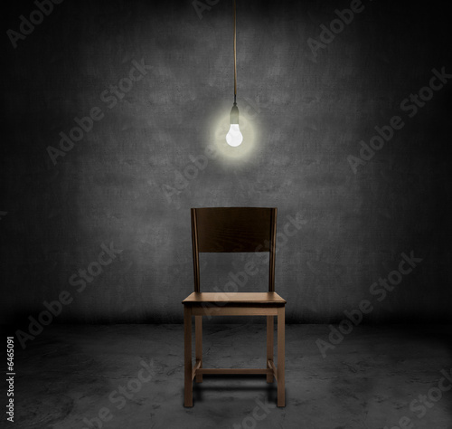 Photography An empty chair and hannging light bulb in a dark room