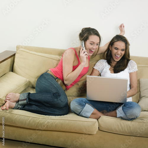  two young girls looking at a laptop laughing calling by phone