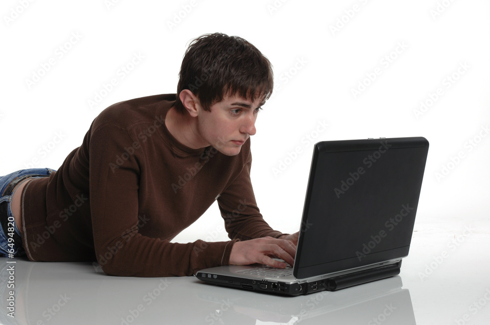 young male intently working on computer while lying on stomach young male intently working on computer while lying on stomach