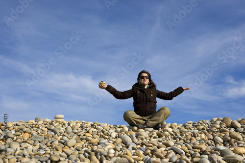 young woman in lotus pose with round peebles in the hand - yoga