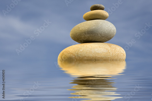 pile of zen round stones with blue sky and water reflexion