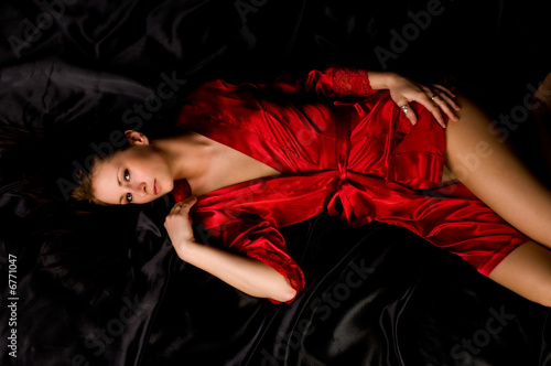 beautiful brunette woman in red robe lying on black satin 