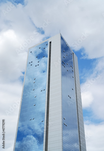 Tall glass building with sky and clouds reflected over its body