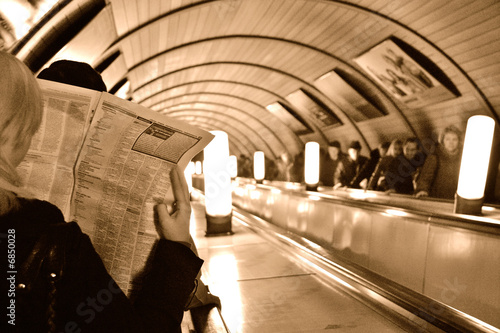The girl reads the newspaper on the escalator