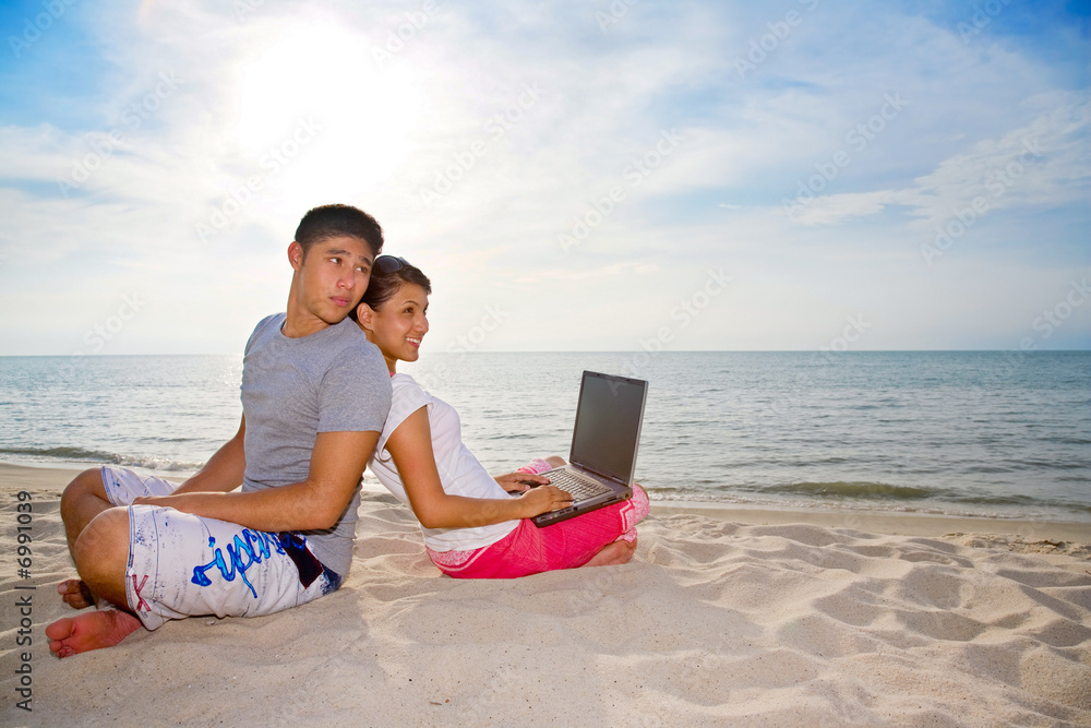 couple relaxing while one of them working on the beach