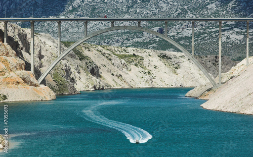 Motorboat sailing under highway bridge in a bay
