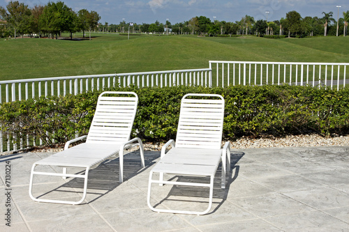 Pool chairs on patio with golf course in background