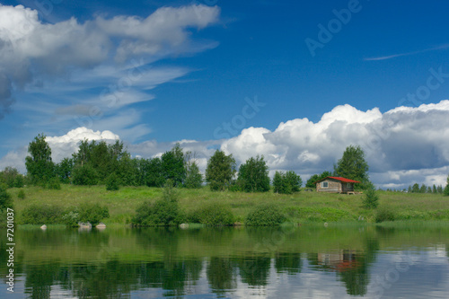 Small loghouse stand in the middle of trees on lake shore   © Artem Sapegin