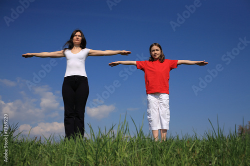 Mother and daughter holding hands up against blue sky 