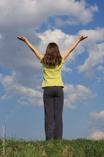 Girl holding hands up against blue sky 