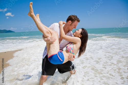 hunky caucasian man carrying gorgeos girl on the beach photo