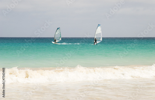 Two windsurfers racing across turquoise seas in Cape Verde.