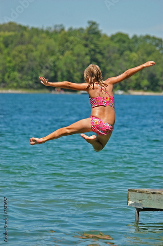 Young Girl Jumps Off Dock into Lake Extending Arms and One Leg