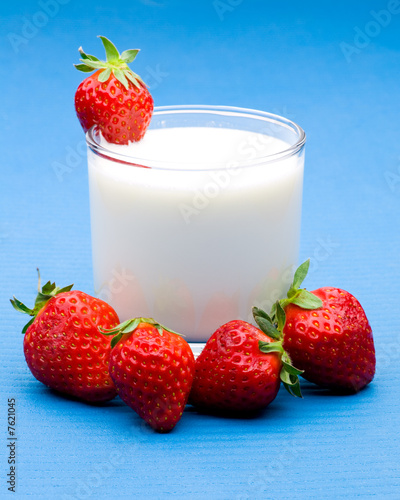 Mehrere Erdbeeren um ein Glas mit Milch