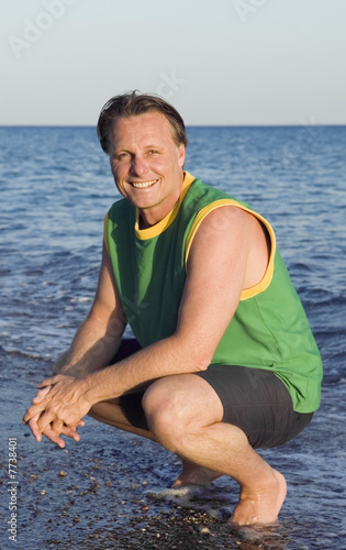 A happy smiling 43 year old man crouching down at the beach