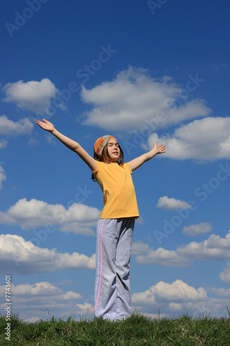 Girl holding hands up against blue sky