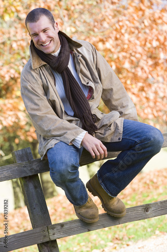 Young man sitting on fence