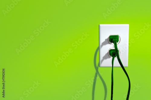 Green power cords in eletric outlet on a green colored wall