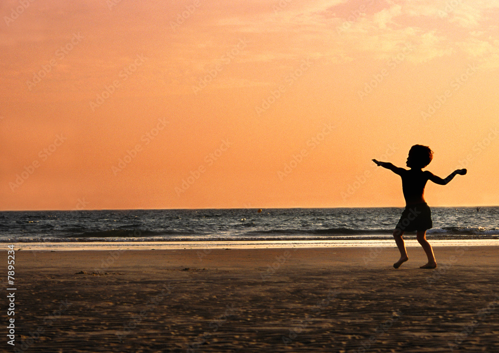 boy throwing sand on beach at sunset