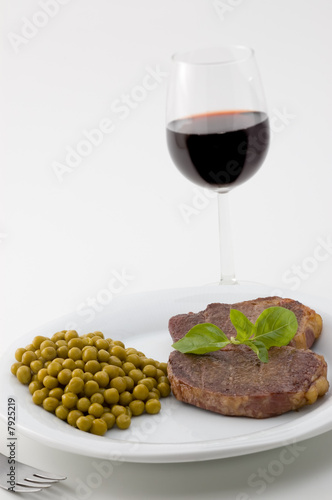 Juicy meat served with peas and basil and red wine glass.