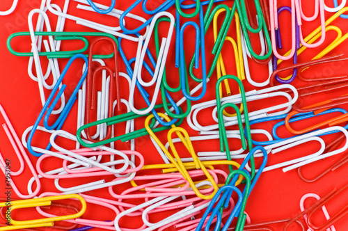 Many colourful paper clips on red background