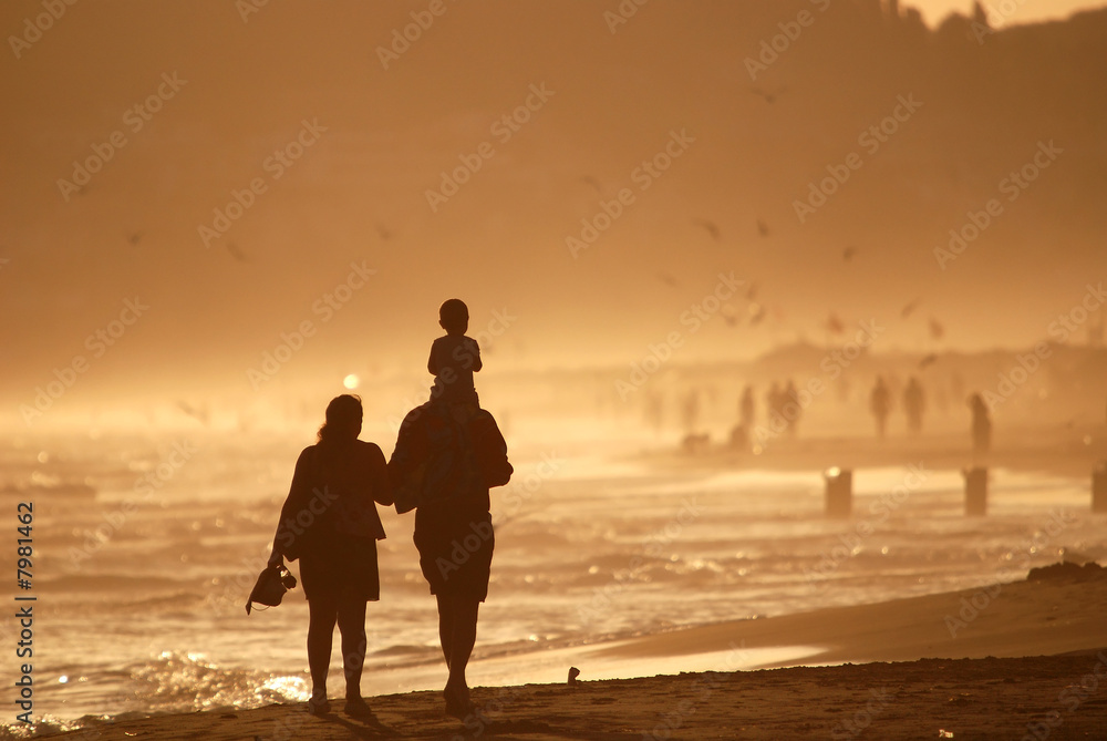 .young family walking on beach at beautiful sunset