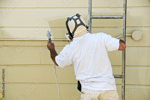 A man on a ladder uses paint spray gun