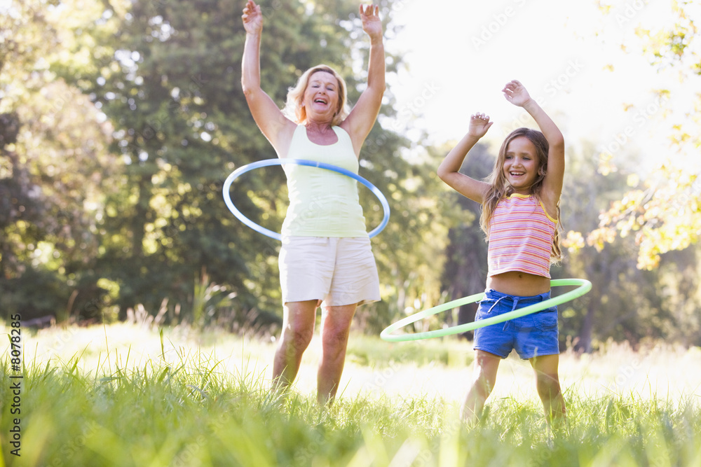 Grandmother and granddaughter at a park hula hooping and smiling
