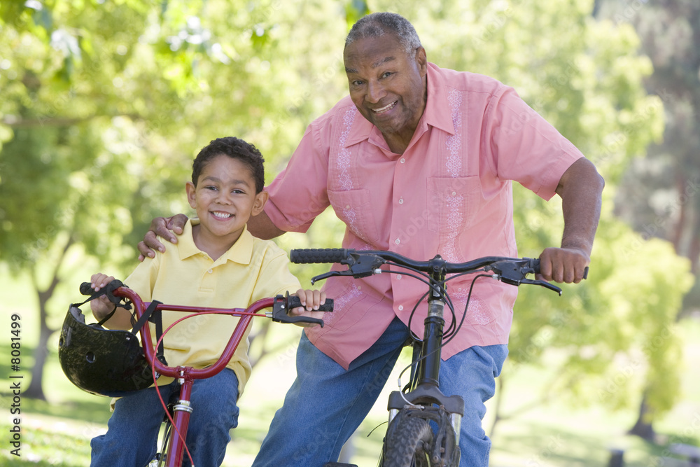 Grandfather and grandson on bikes outdoors smiling Grandfather and grandson on bikes outdoors smiling