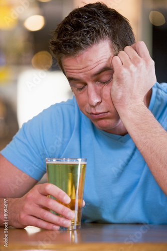 Young man with beer falling asleep at bar