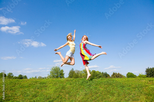 Two happy girls jumping together on green meadow