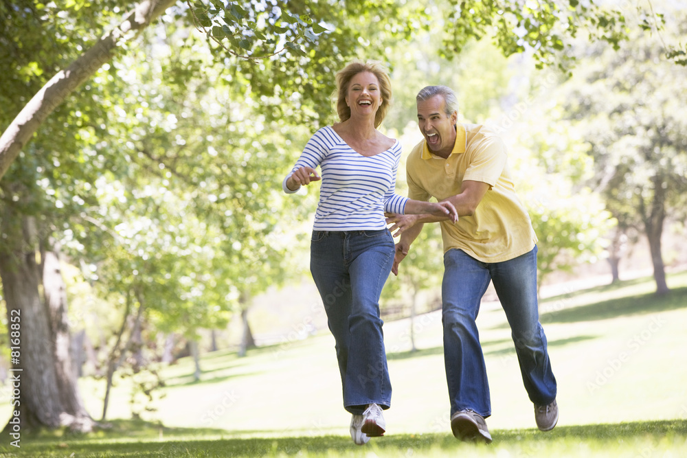 Couple running outdoors in park and smiling Couple running outdoors in park and smiling