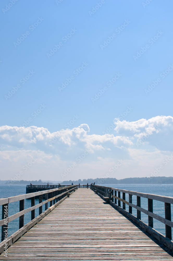 Wooden pier extending into ocean, under hazy blue sky and clouds
