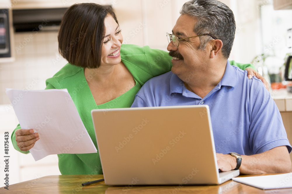 Couple in kitchen with laptop and paperwork smiling Couple in kitchen with laptop and paperwork smiling