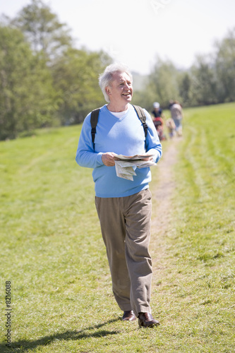 Canvas Print Man walking outdoors holding map smiling with people in backgrou