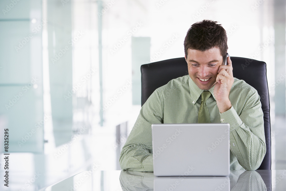 Businessman sitting in office using cellular phone and laptop Businessman sitting in office using cellular phone and laptop