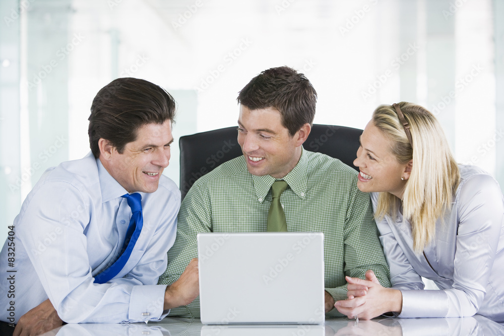 Three businesspeople in a boardroom looking at laptop smiling