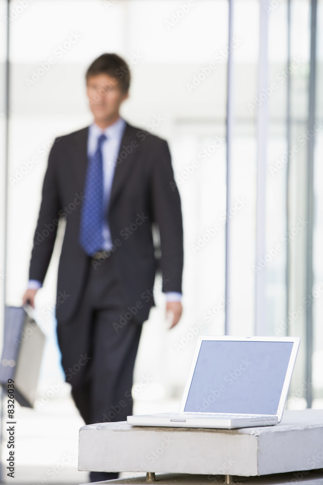 Laptop sitting in office lobby with businessman walking in Laptop sitting in office lobby with businessman walking in