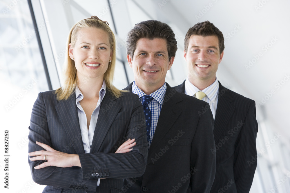 Three businesspeople standing in corridor smiling Three businesspeople standing in corridor smiling
