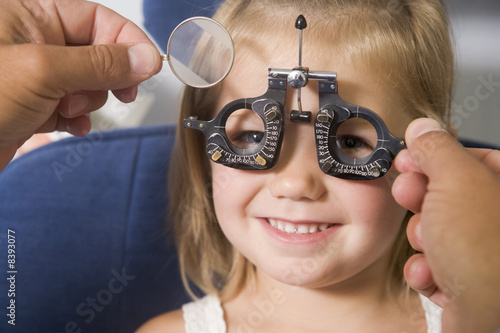 Optometrist in exam room with young girl in chair smiling