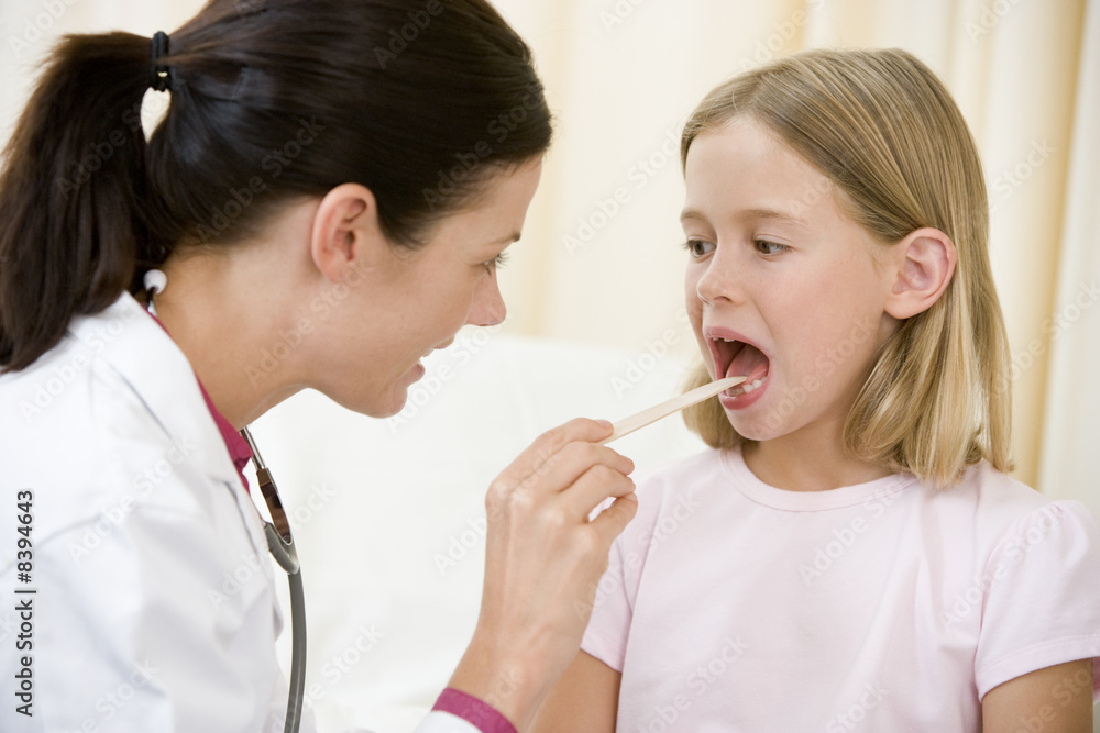 Doctor giving checkup to young girl with tongue depressor in exa Doctor giving checkup to young girl with tongue depressor in exa