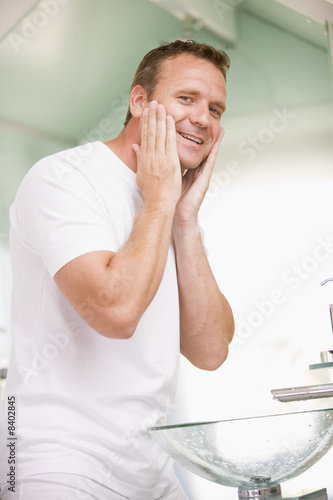 Man in bathroom applying aftershave and smiling